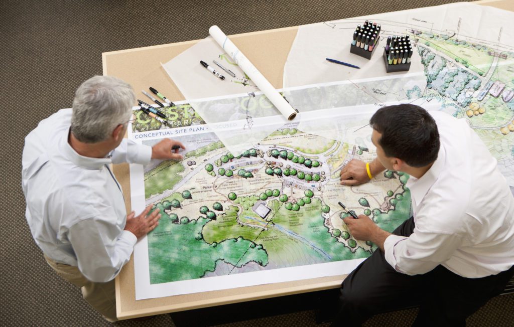 High angle view of two male architects consulting a colorful illustration and landscape rendering on a table in a studio.